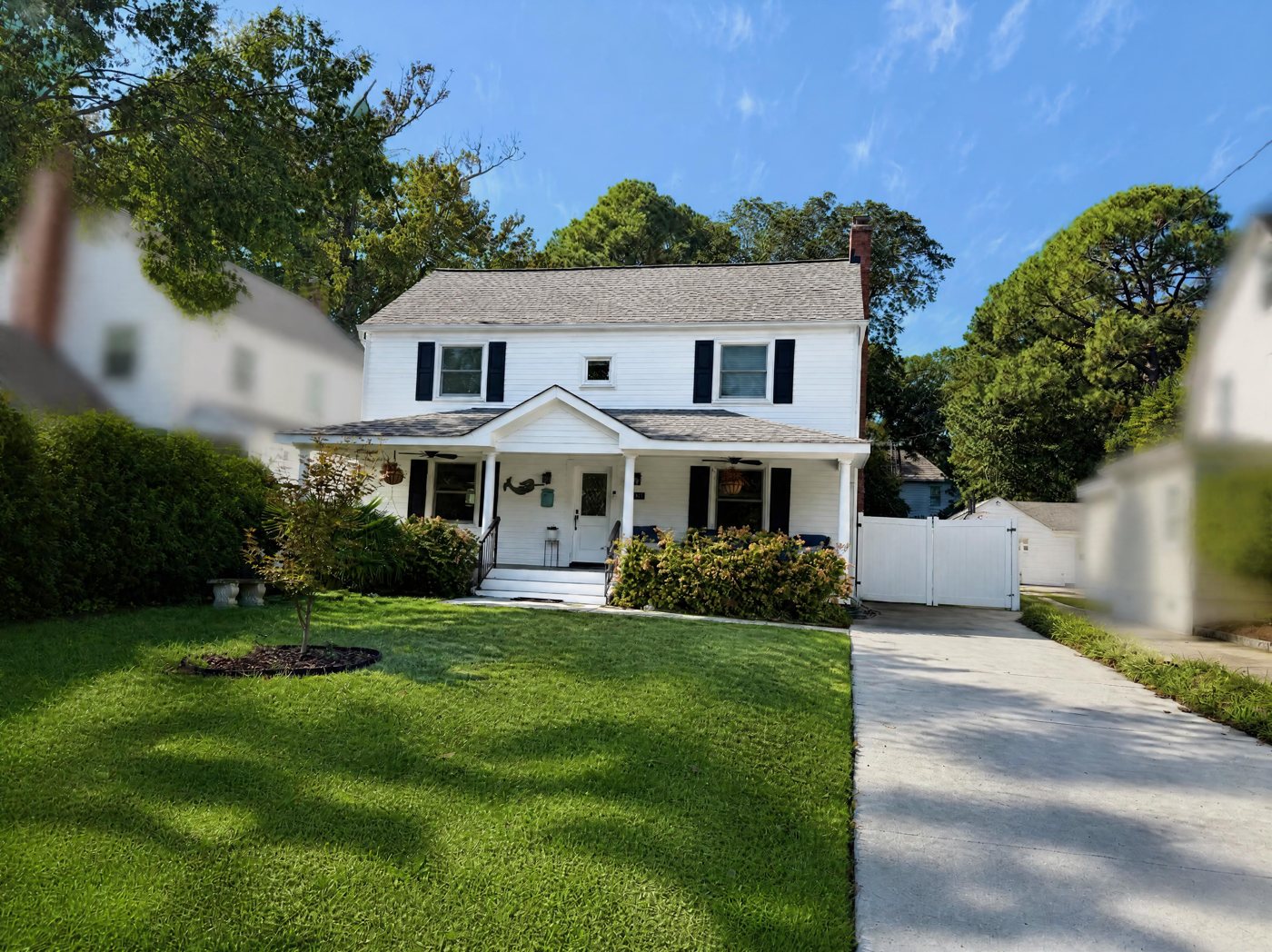 White two-story Norfolk house with black shutters, a covered front porch and a green front lawn